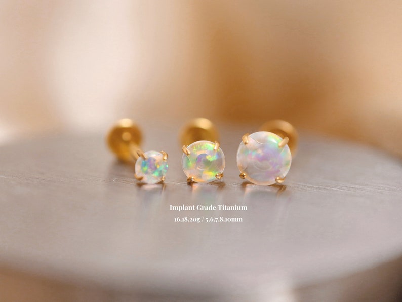 K&ouml;nnte beinhalten: Drei goldene Titan-Opal-Ohrringe mit einem wei&szlig;en Opal-Stein. Die Ohrringe haben einen Durchmesser von 5,6, 7 und 8 Millimetern. Implantat-Grade Titan 16.18.20g / 5.6, 7, 8.10mm