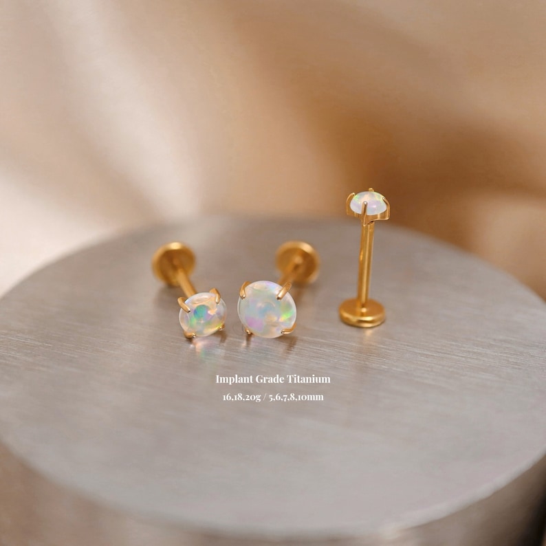 K&ouml;nnte beinhalten: Drei goldene Titan-Opal-K&ouml;rper-Schmuckst&uuml;cke. Zwei sind Ohrstecker mit 5,6, 7,8 und 8,1 mm Opal-Steinen. Der dritte ist eine Barbell mit einem 5,6 mm Opal-Stein. Implantat-Grade Titan 16.18.20g.
