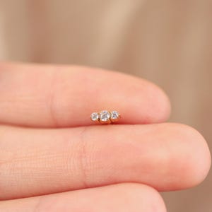K&ouml;nnte beinhalten: Goldener K&ouml;rperschmuck mit drei klaren runden Zirkonia-Steinen.