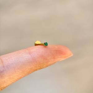 May include: A gold body piercing with a small green gemstone.