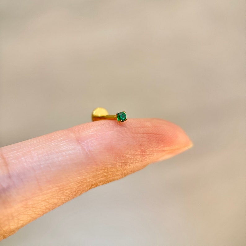 May include: A gold body piercing with a small green gemstone.