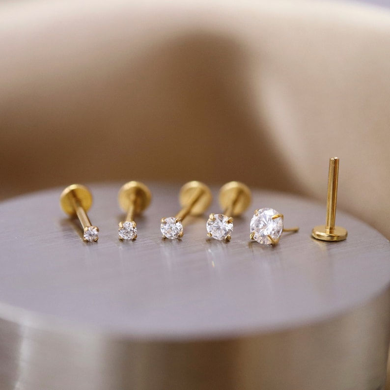 Puede incluir: Un conjunto de seis piezas de joyer&iacute;a corporal de color dorado con piedras preciosas transparentes. La joyer&iacute;a est&aacute; dispuesta sobre una superficie plateada.