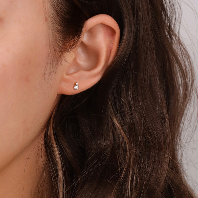 Puede incluir: Primer plano de una oreja con un peque&ntilde;o pendiente de bot&oacute;n de piedra preciosa transparente.