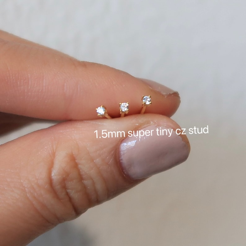 Pu&ograve; includere: Tre perni per il naso in oro con minuscoli zirconi cubici trasparenti. I perni sono di 1,5 mm e sono mostrati su un dito.