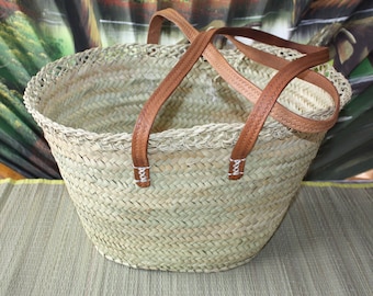 Puede incluir: Bolso tote de paja tejida con asas de cuero marrón. El bolso tiene forma redondeada y una construcción robusta. Las asas están cosidas con hilo blanco en la base. Adecuado para llevar comestibles u otros artículos.