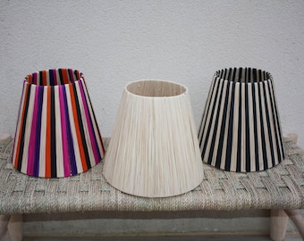 May include: Three lampshades with different striped patterns. The lampshades are made of woven material and have a conical shape. The lampshades are sitting on a woven surface.