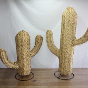 Puede incluir: Dos esculturas de cactus de mimbre tejido con soportes de metal negro. El cactus m&aacute;s grande mide aproximadamente 76 cm de alto y el m&aacute;s peque&ntilde;o aproximadamente 46 cm.