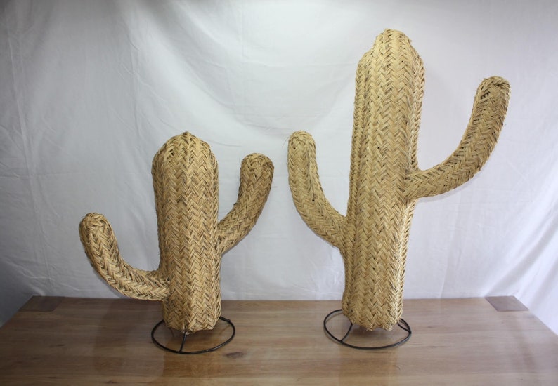 Puede incluir: Dos esculturas de cactus de mimbre tejido con soportes de metal negro. El cactus m&aacute;s grande mide aproximadamente 76 cm de alto y el m&aacute;s peque&ntilde;o aproximadamente 46 cm.