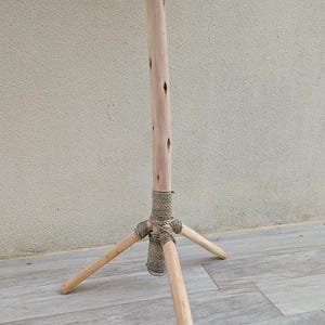Puede incluir: Un soporte de tr&iacute;pode de madera con un acabado natural. El soporte tiene tres patas que est&aacute;n conectadas a un poste central con una envoltura de cuerda.