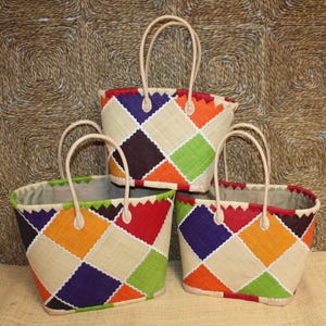 Peut inclure: Trois sacs fourre-tout tissés colorés avec des motifs géométriques. Chaque sac présente un motif patchwork de carrés orange, verts, rouges, violets et beiges. Ils ont des poignées beiges et un fond neutre.