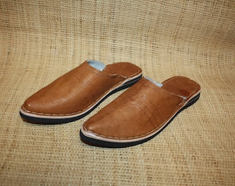 May include: A pair of brown leather slippers with a pointed toe and a closed back. The slippers have a white stitching detail around the edges and a black rubber sole.