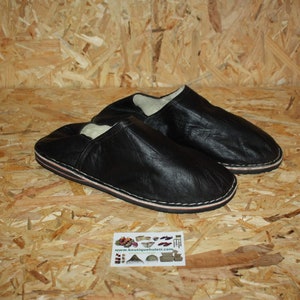 Op de afbeelding: Een paar zwarte leren slippers met een witte voering. De slippers hebben een eenvoudig ontwerp en zijn gemaakt van zacht leer.