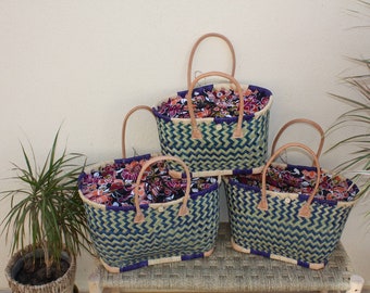 May include: Three woven baskets with leather handles and colorful fabric lining. The baskets are stacked on a woven surface.
