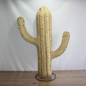 Puede incluir: Una gran escultura de cactus de paja tejida con una base marr&oacute;n. El cactus est&aacute; hecho de materiales naturales y tiene un estilo r&uacute;stico del suroeste.