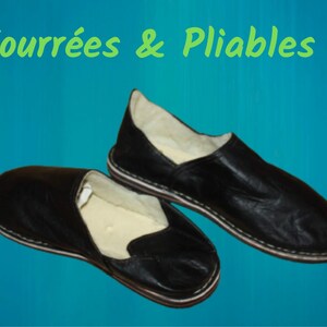 Op de afbeelding: Twee paar zwarte leren slippers met een witte voering. De slippers zijn gevoerd met wit bont en hebben een gestikte naad rond de rand. De tekst "Fourr&eacute;es & Pliables!" staat in het groen op een blauwe achtergrond.