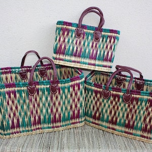 Peut inclure: Trois sacs fourre-tout tissés. Les sacs ont une forme rectangulaire avec un motif tissé vert, violet et beige. Ils ont des poignées et des accents en cuir marron. Les sacs sont empilés sur une surface tissée.