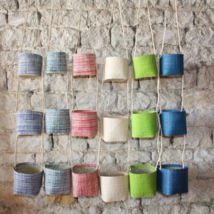 Peut inclure: Une collection de 18 paniers suspendus en tissu tissé de différentes couleurs et motifs, notamment bleu, vert, rouge et blanc. Les paniers sont suspendus à un mur de briques.