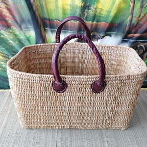 May include: A rectangular woven basket with two brown leather handles. The basket is made of natural materials and has a light brown colour.