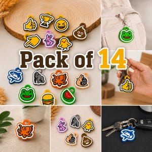 Könnte beinhalten: Ein Set aus 14 bunten Silikonanhängern mit verschiedenen Motiven, darunter ein Daumen hoch, ein Pokal, ein lachendes Emoji, ein Kackhaufen-Emoji, ein Hase, ein Küken, ein Hai, ein Gorilla, ein Oktopus, eine Schnecke, ein Burger, eine Wassermelone und ein grüner Frosch.