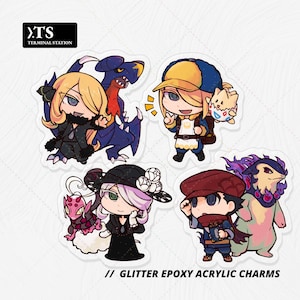 May include: Four glitter epoxy acrylic charms featuring chibi-style characters and creatures. The designs include a blonde character with a blue dragon, a character with a yellow cap and a small egg creature, a character with a black hat and pink creature, and a character with a red cap and a purple-flamed creature. Text reads TERMINAL STATION.