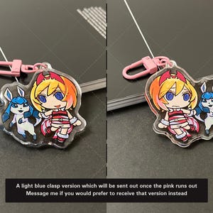May include: A clear acrylic charm featuring a cartoon character with orange hair and a blue creature, attached to a pink plastic lobster clasp. The text reads: A light blue clasp version which will be sent out once the pink runs out. Message me if you would prefer to receive that version instead.