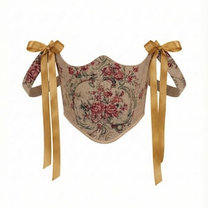 May include: A beige corset with a floral tapestry design featuring red and pink roses. The corset has gold-colored ribbon straps tied into bows at the shoulders. The garment is designed with a curved neckline.