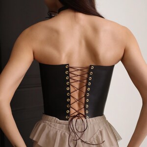 Back view of model wearing a custom made brown leather corset with lace-up back, styled as a renaissance corset body and pirate corset for dress. This plus size friendly corset defines the waist and is ideal for steampunk corset looks, victorian or renfair outfits, and western style fashion. A handmade korsett shown paired with layered beige skirt. Black and brown waist corset options available.