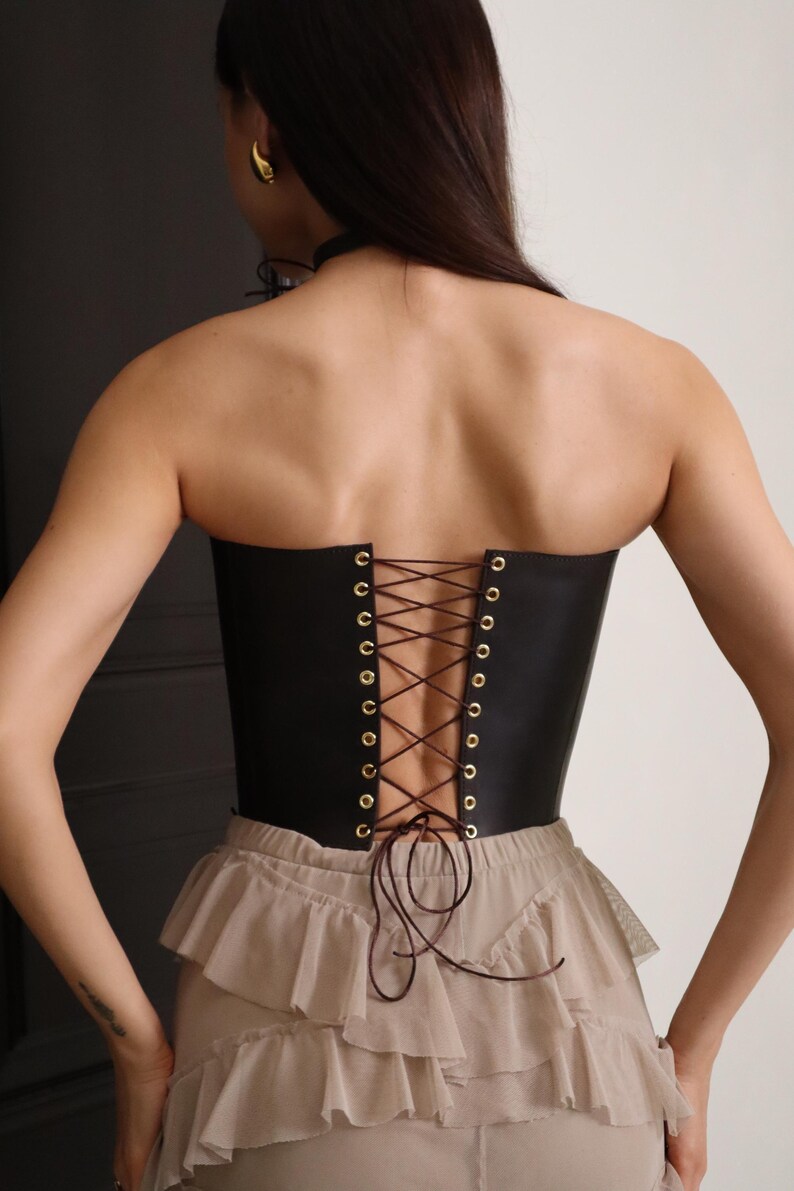 Back view of model wearing a custom made brown leather corset with lace-up back, styled as a renaissance corset body and pirate corset for dress. This plus size friendly corset defines the waist and is ideal for steampunk corset looks, victorian or renfair outfits, and western style fashion. A handmade korsett shown paired with layered beige skirt. Black and brown waist corset options available.