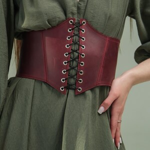 A close-up of a person wearing a green dress with a red corset belt.