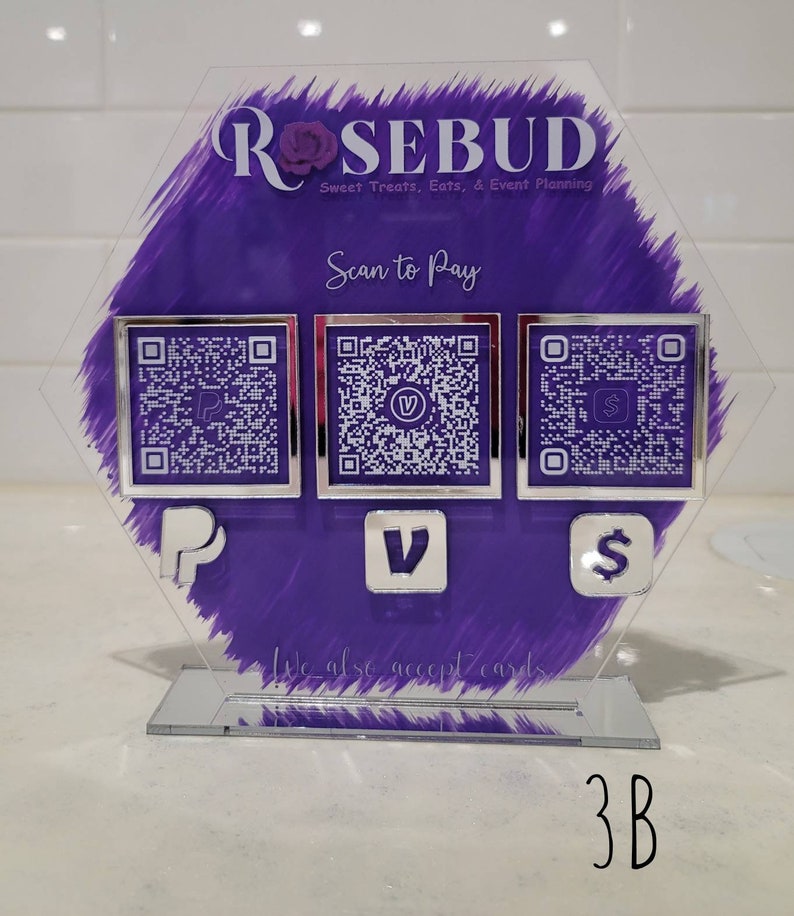 Pode incluir: Uma placa de acr&iacute;lico roxa com o texto "ROSEBUD Sweet Treats, Eats, & Event Planning" e o texto "Scan to Pay". A placa tem tr&ecirc;s c&oacute;digos QR quadrados com os logotipos do PayPal, Venmo e Square. A placa tamb&eacute;m tem o texto "We also accept cards." e o texto "3B".