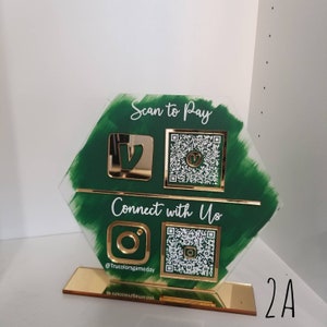 Pode incluir: Uma placa hexagonal de acr&iacute;lico verde e dourado com dois c&oacute;digos QR e logotipos do Venmo e Instagram. A placa diz "Scan to Pay" e "Connect with Us" com o nome de usu&aacute;rio do Instagram "@Trucolorsgameday".