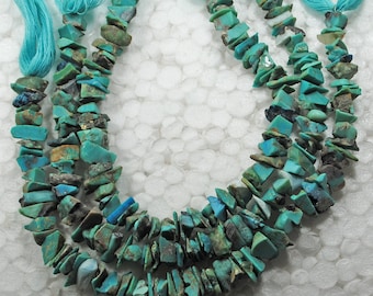 May include: A strand of turquoise gemstone beads, featuring a mix of light and dark blue hues. The beads are irregular in shape and size, with some having a rough, chipped texture. The beads are strung on a turquoise thread.