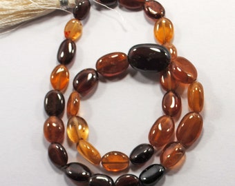 May include: Two strands of polished, oval-shaped gemstones in shades of amber, brown, and black. The beads are strung together, with a white tassel at the top. The gemstones have a glossy finish.