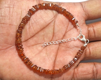 May include: A bracelet featuring small, faceted, orange-brown gemstones strung together. The bracelet has a silver-colored chain and clasp. The gemstones are a warm, earthy color, and the bracelet is shown on a hand.
