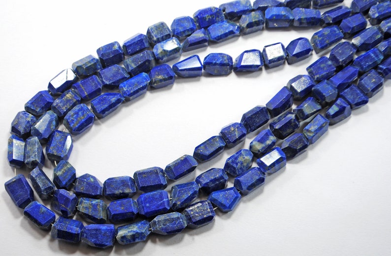 May include: A strand of faceted lapis lazuli beads, each bead is a deep blue with white and gold flecks. The beads are strung on a clear thread.