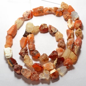 May include: A strand of rough, natural opal beads in various shades of orange, red, and white. The beads are irregular in shape and size, and some have a translucent appearance.