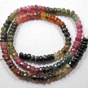 Könnte beinhalten: Eine Strähne aus mehrfarbigen Turmalinperlen. Die Perlen sind facettiert und haben einen Regenbogen an Farben, darunter Pink, Grün, Schwarz und Braun.