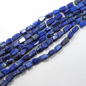 May include: A strand of dark blue lapis lazuli gemstone beads with a faceted, rectangular shape. The beads are strung on a clear thread.
