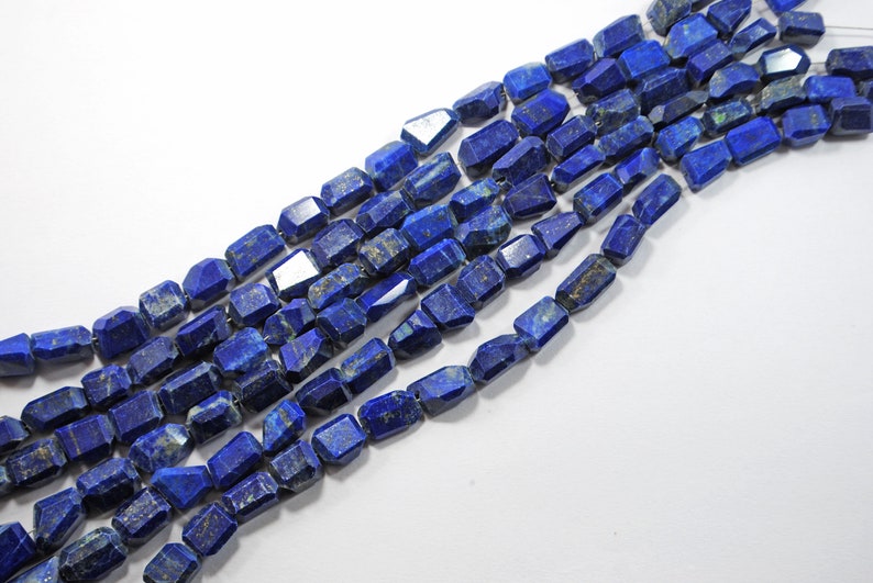 May include: A strand of dark blue lapis lazuli gemstone beads with a faceted, rectangular shape. The beads are strung on a clear thread.