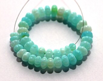May include: Strand of light blue and green gemstone beads. The beads are oval-shaped with carved details, strung on a thin wire. The beads vary in color from light green to a vibrant turquoise.