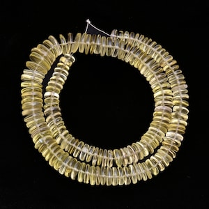 May include: A strand of light yellow citrine gemstone beads. The beads are faceted and have a slightly oval shape. The beads are strung on a white thread and are arranged in a double row.