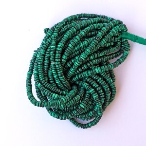 May include: A strand of green malachite beads, each bead is round and slightly flattened. The beads are strung on a thin cord and are piled together in a loose heap.