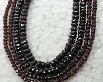 May include: A strand of dark red faceted gemstone beads. The beads are strung on a clear thread and are arranged in a circular pattern.