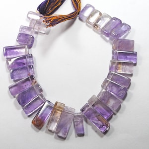 May include: A strand of purple and clear amethyst gemstone beads, each bead is rectangular and faceted. The beads are strung on a cord with a purple tassel.