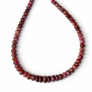 May include: A necklace composed of numerous small, faceted, round beads in varying shades of deep red, maroon, and dark pink. The beads are strung together in a continuous strand, displaying a polished, reflective surface with natural color variations.