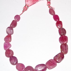 Può includere: Una collana di perle di pietre preziose rosa con un fiocco rosa ad ogni estremità. Le perle sono lisce e di forma ovale.