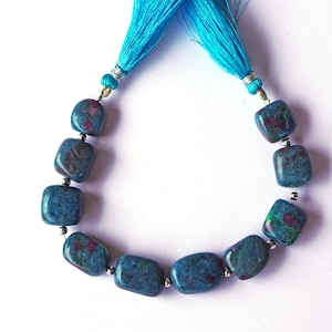 May include: A strand of blue-green gemstone beads with red inclusions, strung together with silver-colored spacers. The strand is attached to a pair of bright turquoise tassels. The beads have a polished, rounded rectangular shape.
