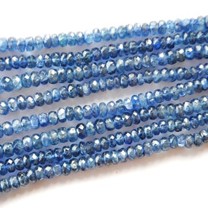 Può includere: Una collana di perline di pietre preziose blu. Le perline sono sfaccettate e hanno una forma leggermente irregolare. Le perline sono infilate su un filo trasparente.