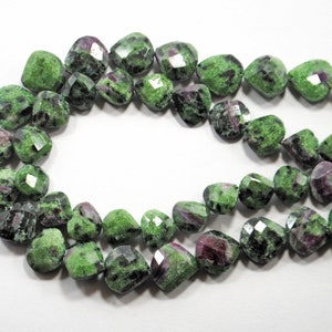 Pode incluir: Um fio de contas de pedras preciosas verdes e rosadas. As contas são facetadas e têm a forma de um coração. As contas são enfiadas em um fio e estão prontas para serem usadas para fazer joias.