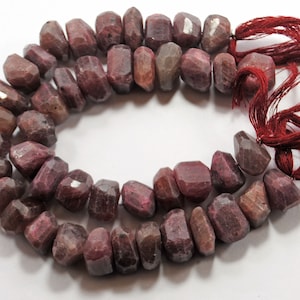 May include: A strand of faceted ruby beads with a red tassel. The beads are a deep red color and have a slightly irregular shape. The tassel is made of a soft, silky material.